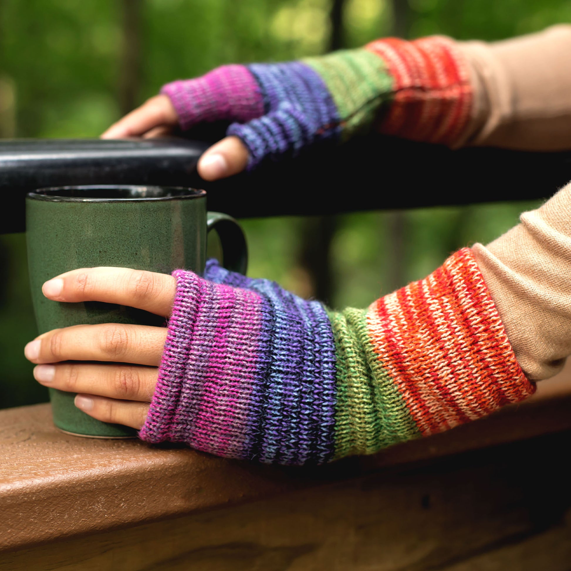 Colorful knitted fingerless gloves holding a green mug outdoors. Made from alpaca wool