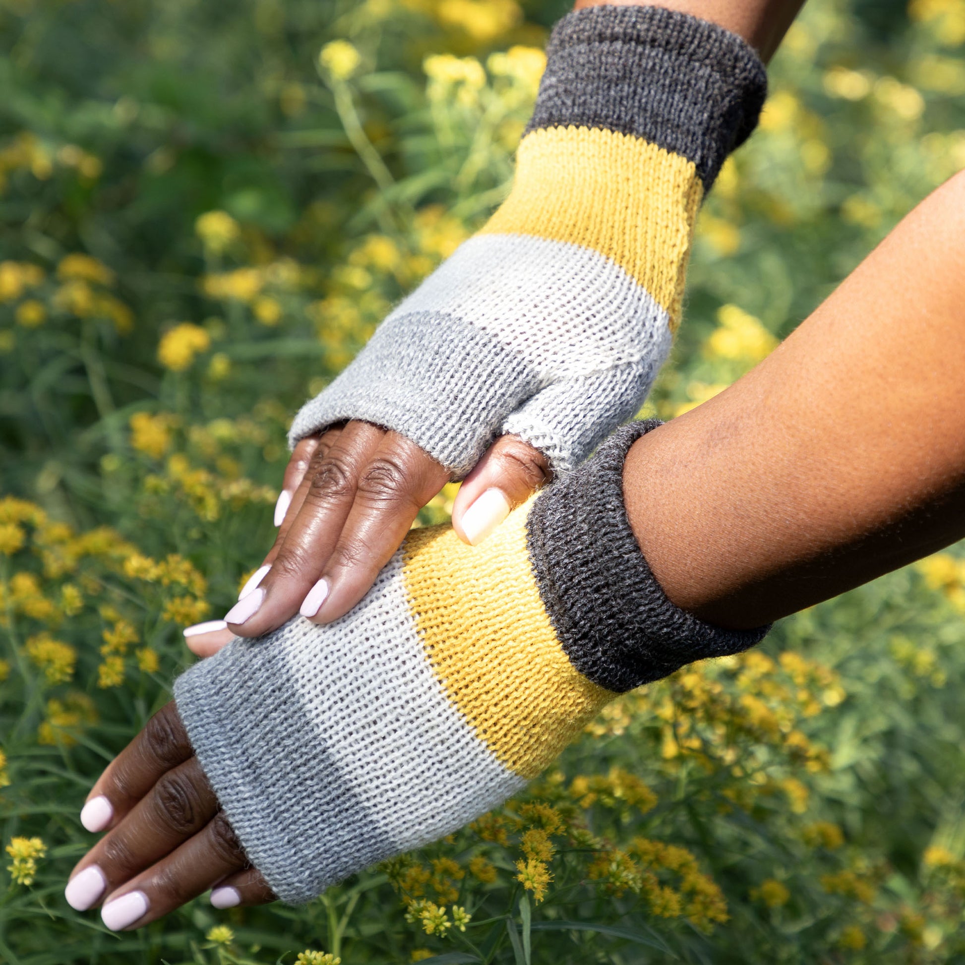 Color-blocked fingerless gloves worn by a person against a natural background with yellow flowers.