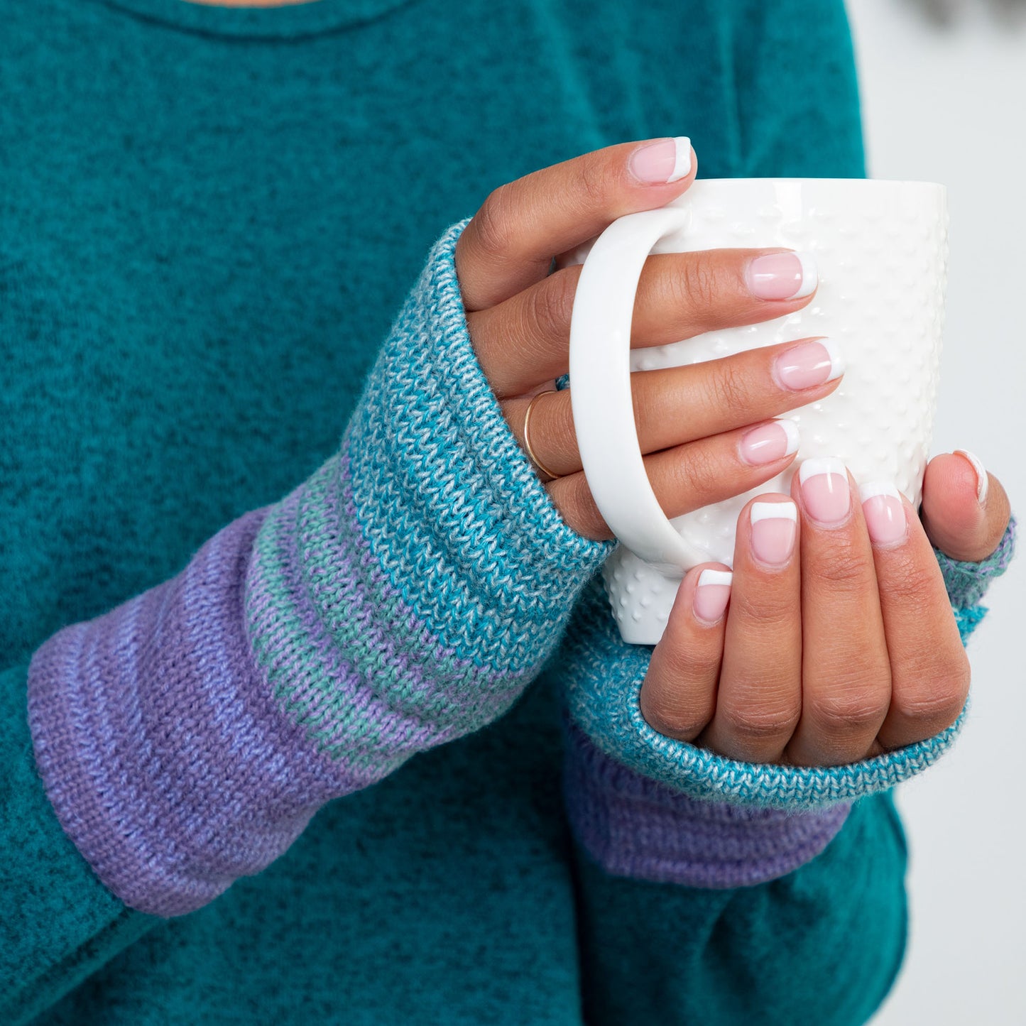 Person wearing colorful fingerless gloves holding a white mug.