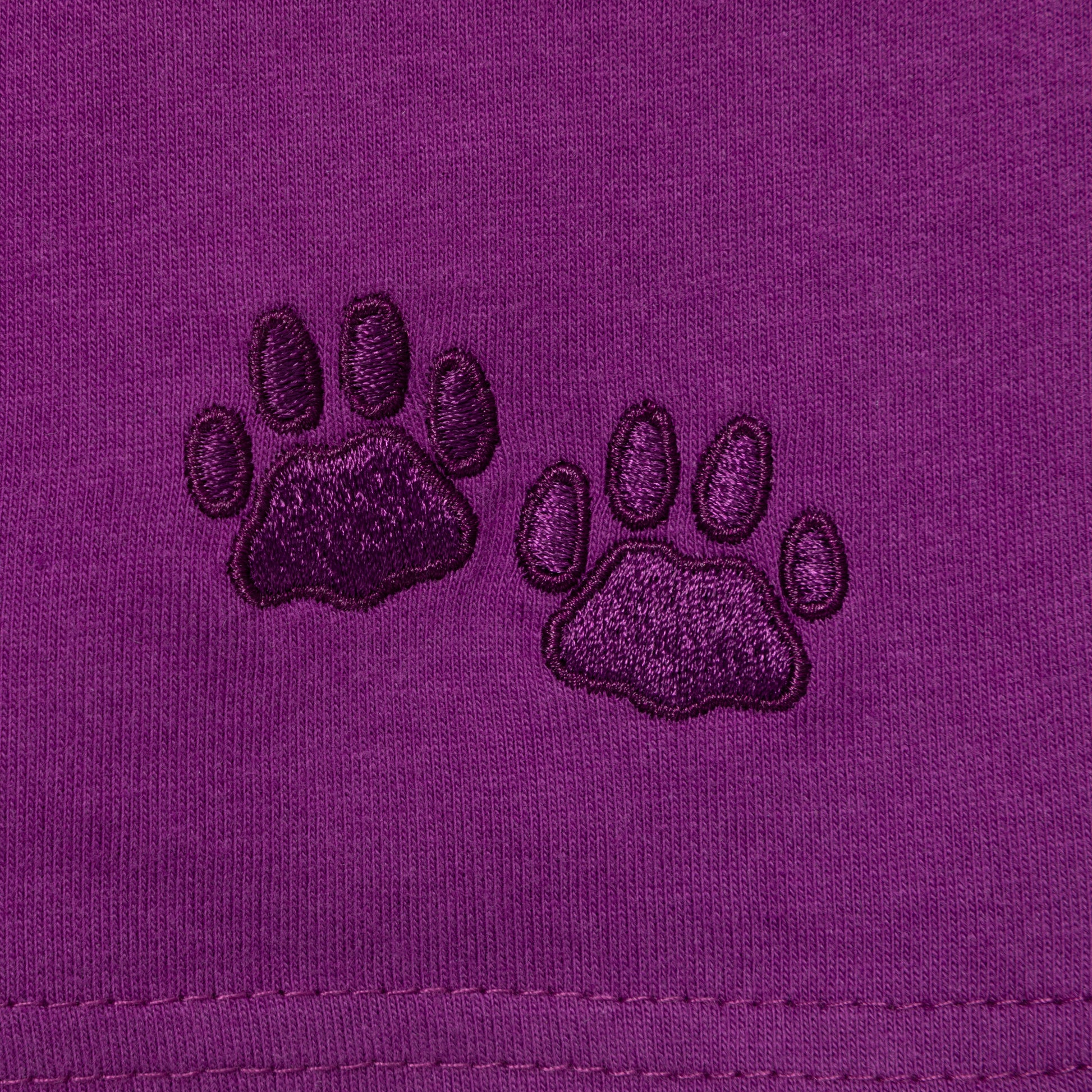 Two embroidered paw prints on a purple fabric background