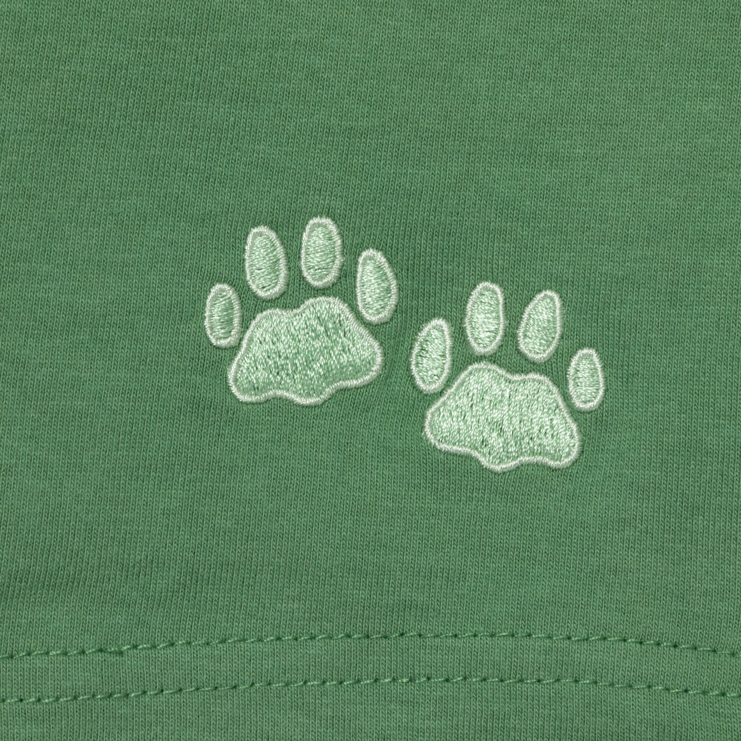 Two light green embroidered paw prints on a green fabric background