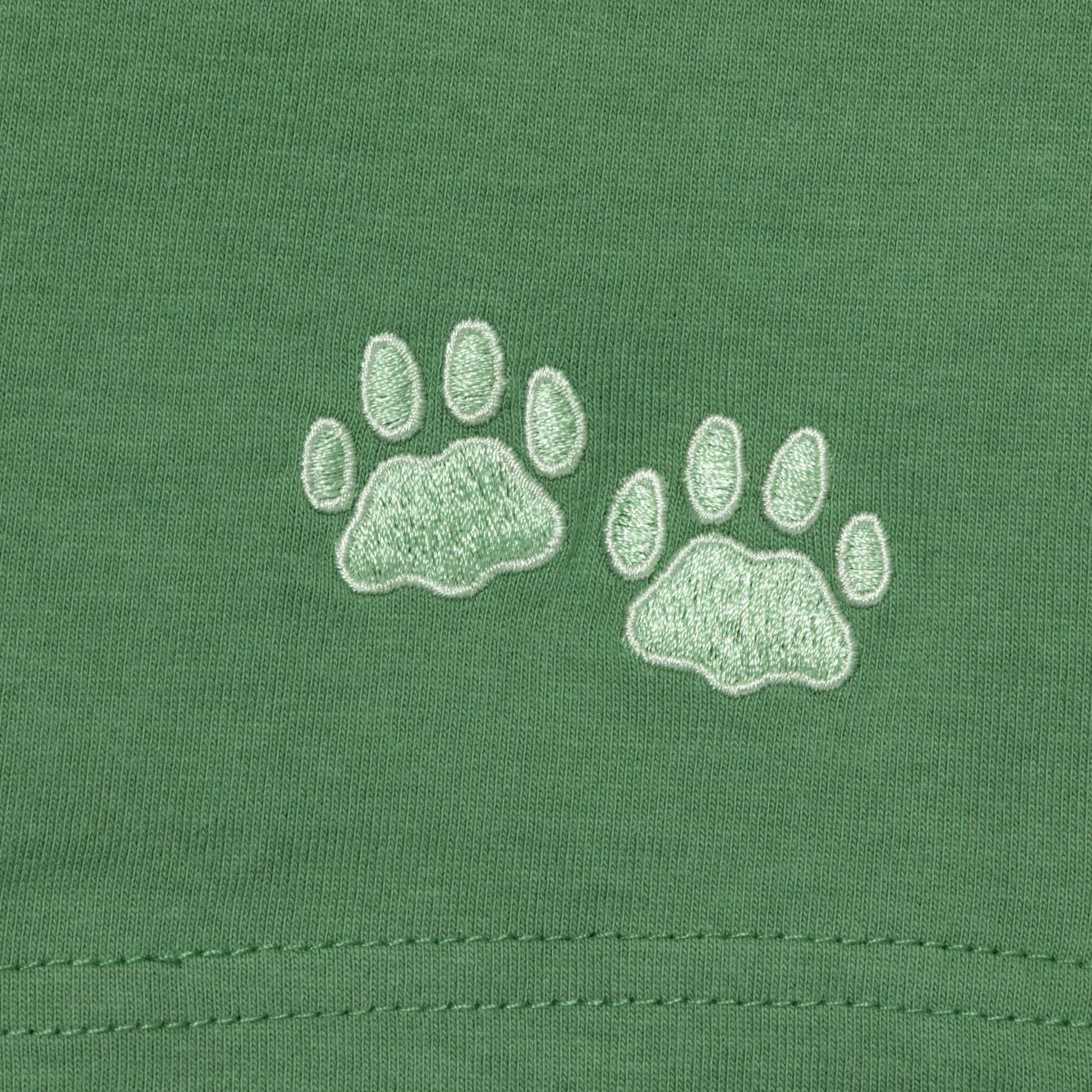Two light green embroidered paw prints on a green fabric background