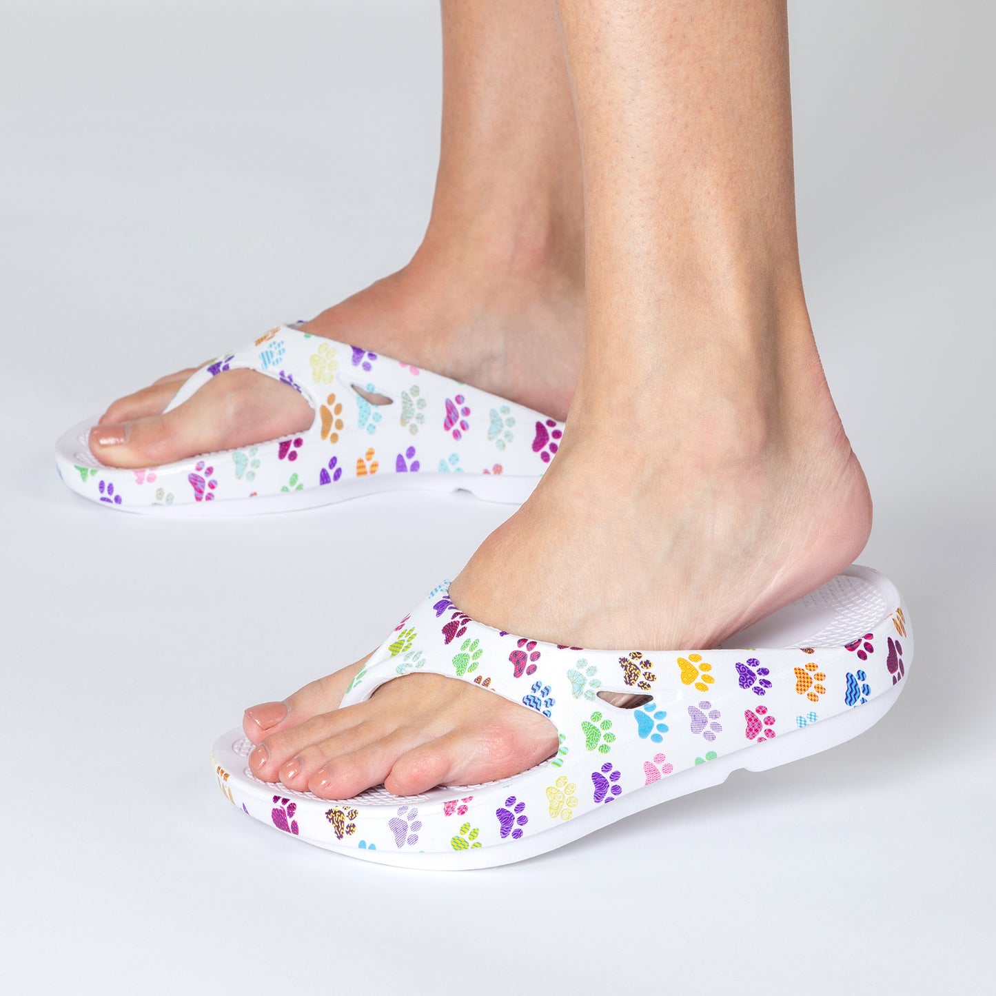 White sandals with colorful paw prints worn by a person on a light gray background