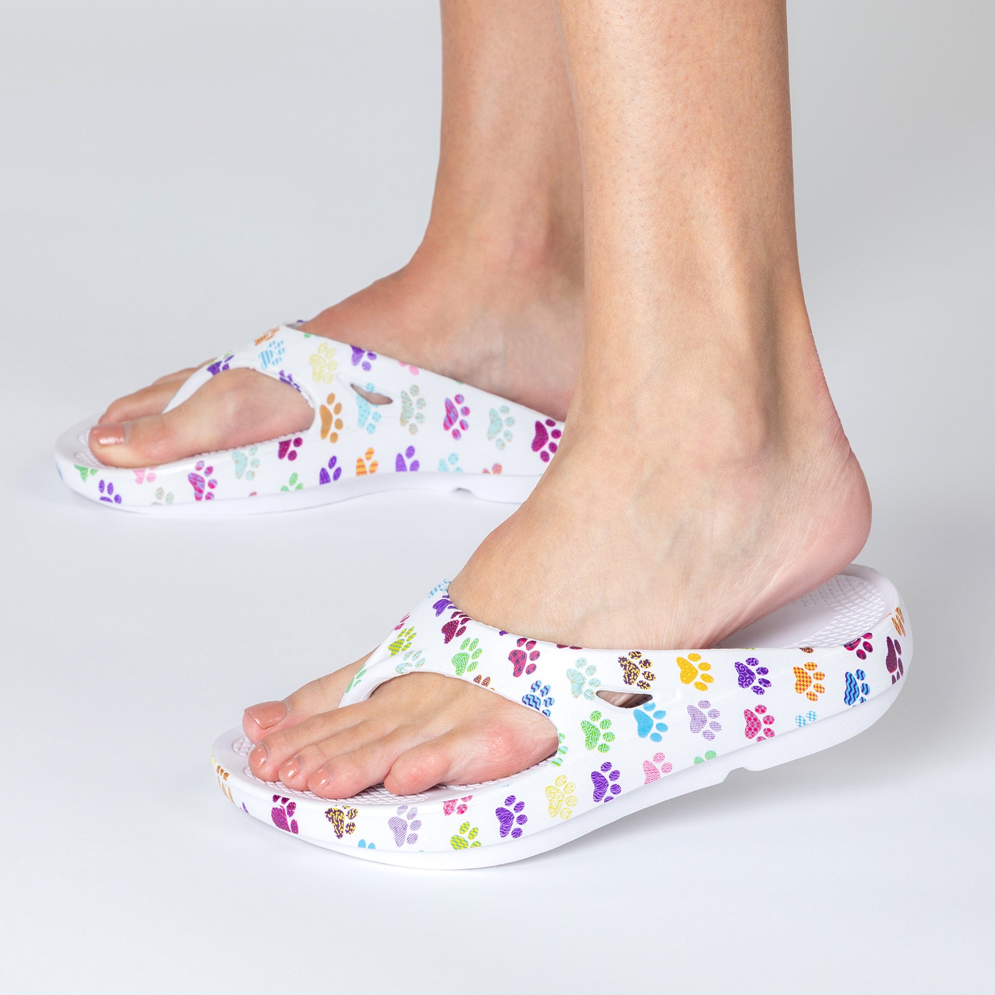 White sandals with colorful paw prints worn by a person on a light gray background