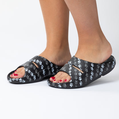 Black sandals with paw print pattern worn by a person on a white background