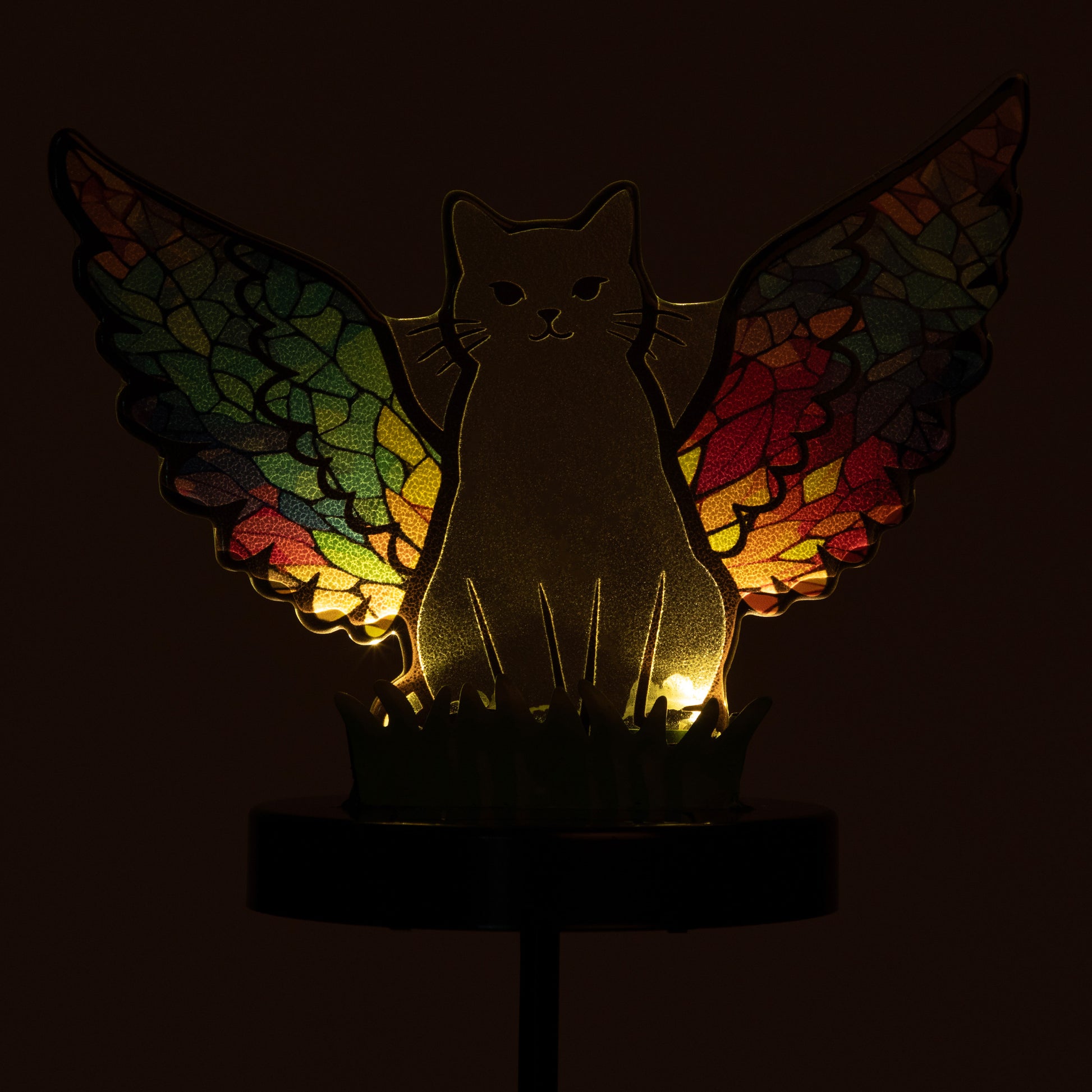 Cat silhouette with mosaic angel wings on a garden stake, against a dark background so the solar light softly glows.