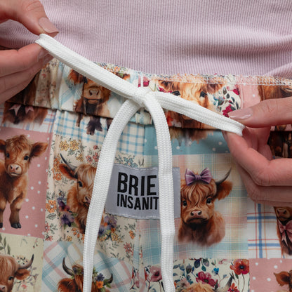 Quilted lounge pants with cow illustrations and a visible brand label, held by hands.