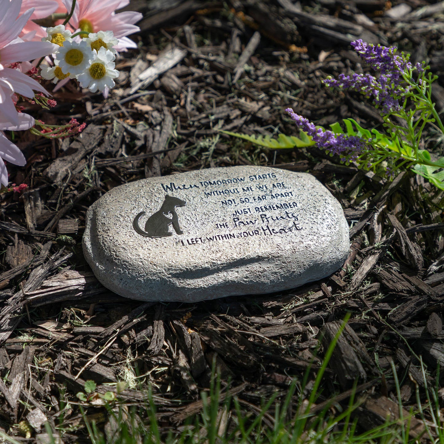Decorative stone with text and dog silhouette on mulch with flowers