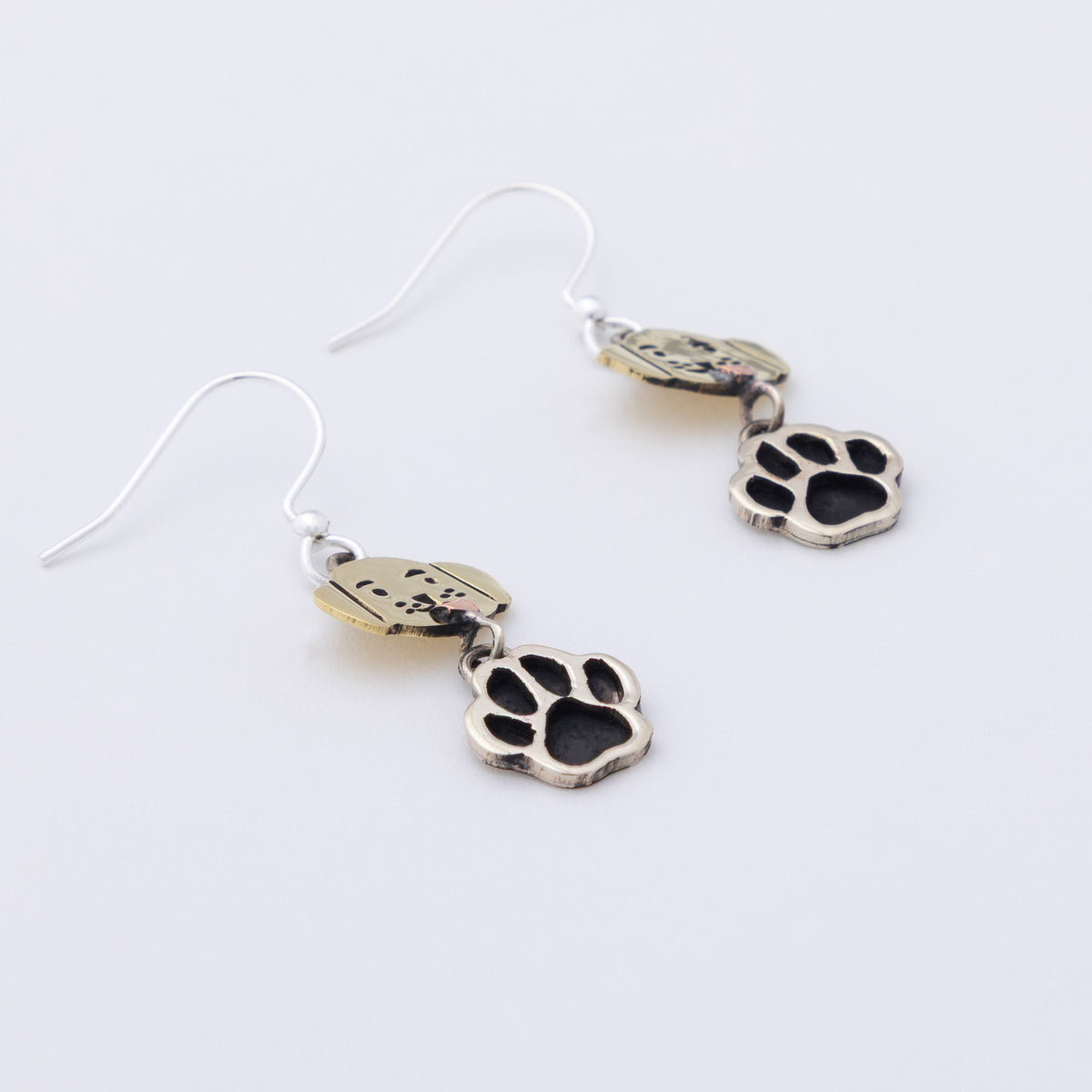 A pair of silver-toned dangle earrings featuring a small dog-shaped charm and a larger paw print charm, displayed on a clean white background.