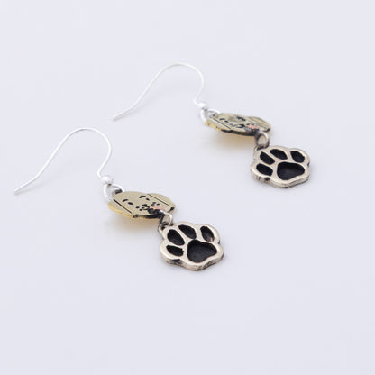 A pair of silver-toned dangle earrings featuring a small dog-shaped charm and a larger paw print charm, displayed on a clean white background.