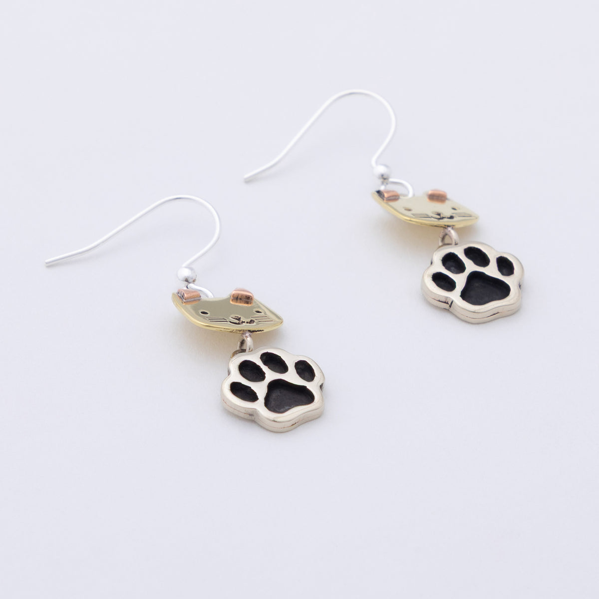 A pair of silver-toned dangle earrings featuring cat head charms and dangling paw prints, displayed on a clean white background.