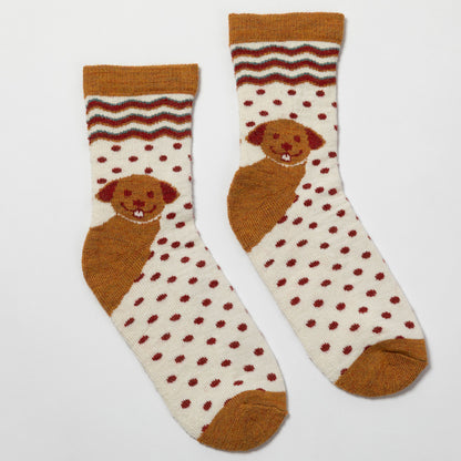 A pair of crew socks with a cream background, dark red polka dots, a brown dog motif, and a wavy stripe pattern near the cuff, displayed on a light gray background.