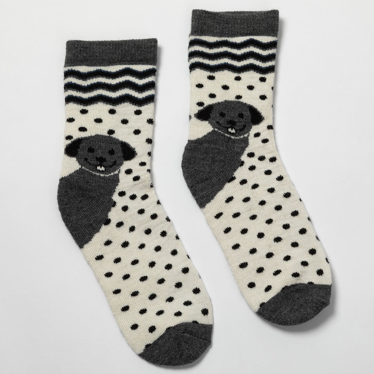 A pair of crew socks with a cream base, black polka dots, dark gray toe/heel/cuff areas, and a stylized dog face motif on the front.