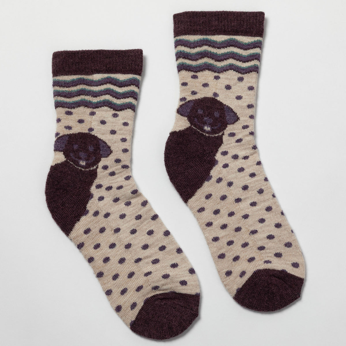 A pair of crew socks with a beige and dark brown polka dot pattern, featuring a knitted pug face on the side and a wavy stripe pattern near the top cuff.