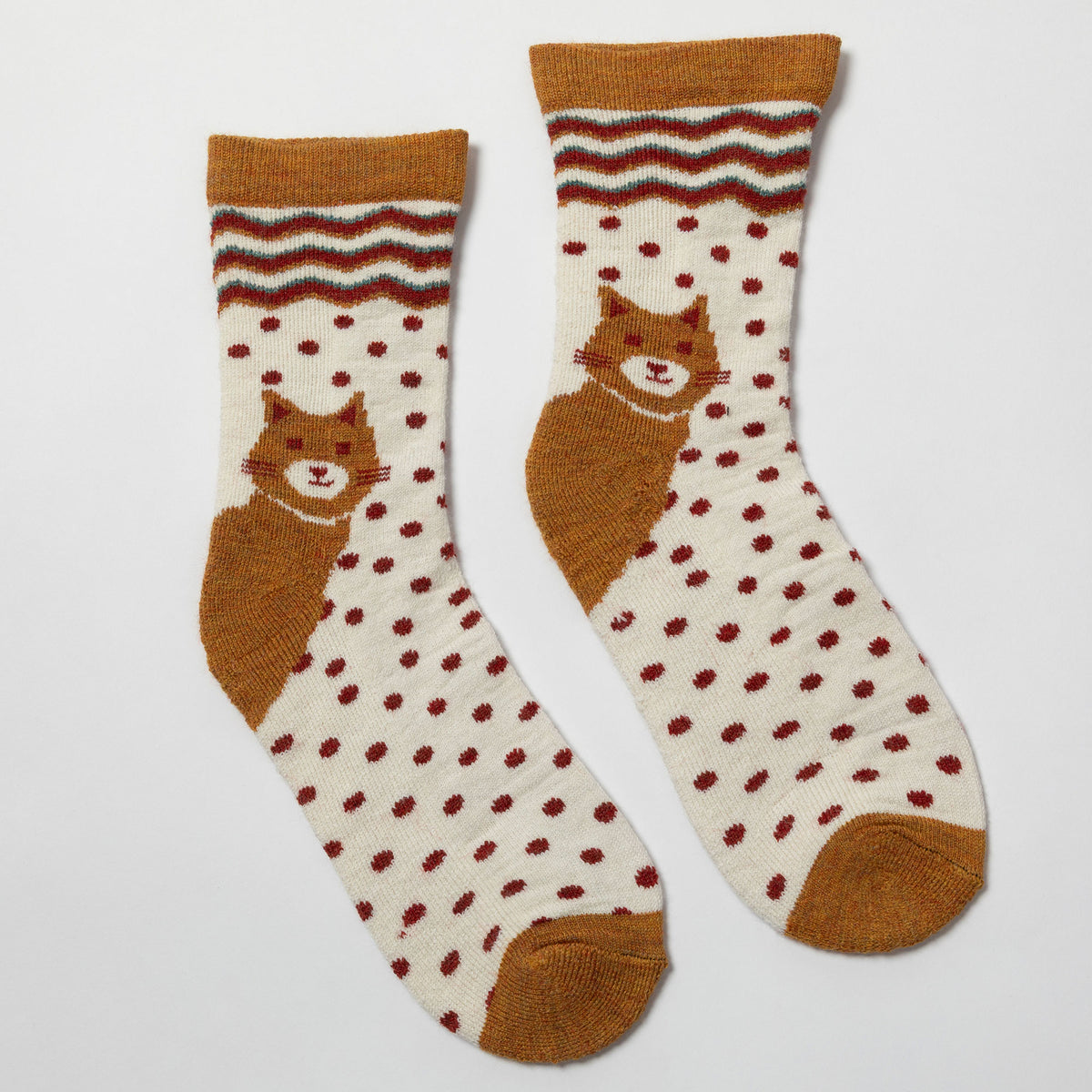 A pair of crew socks with a cream base, brown polka dots, a brown cat graphic, and a brown chevron pattern at the top, displayed on a light gray background.