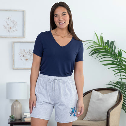 Woman wearing a navy blue shirt and gray shorts with a sea turtle design in a living room setting.