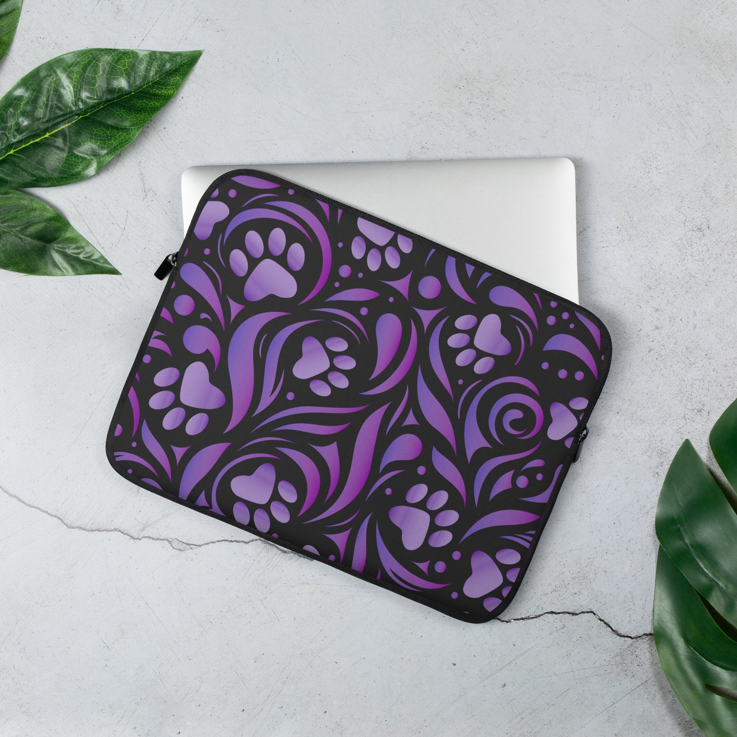 Laptop Sleeve bag designed with purple paw prints and swirls with black accents. palm tree leaves lay beside it.