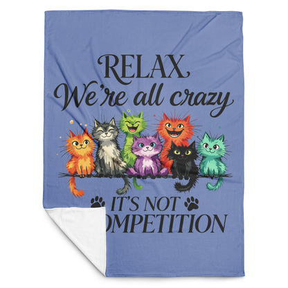 A blue throw blanket with a white sherpa lining, featuring a graphic of seven colorful cartoon cats and the text 'RELAX We're all crazy IT'S NOT COMPETITION'.