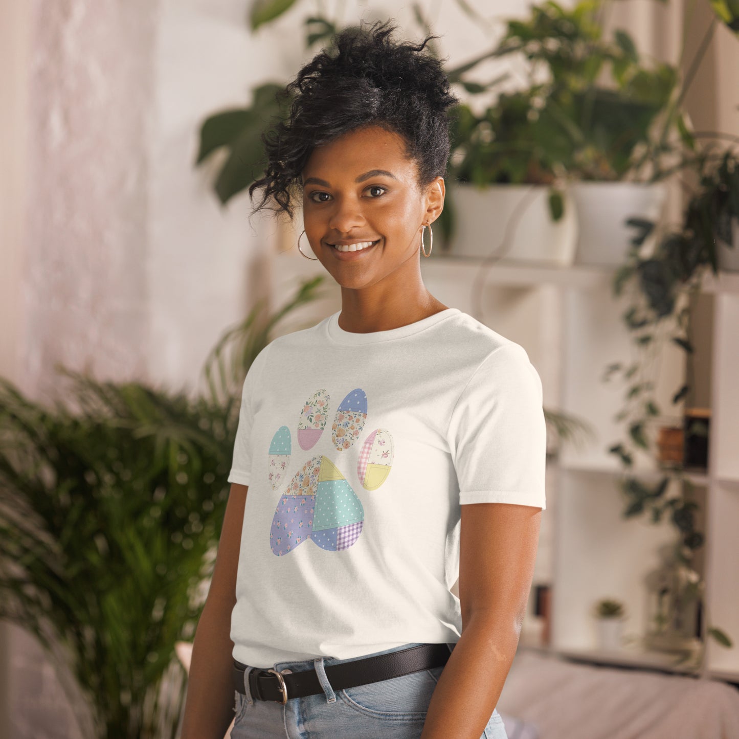 Person wearing a white t-shirt with quilted paw print printed on it, standing in a room with plants.