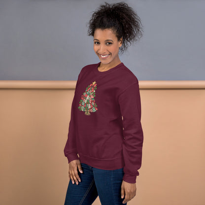 A woman wearing a maroon crewneck sweatshirt with a colorful Christmas tree graphic on the front, paired with blue jeans, standing against a two-tone gray and beige studio background.