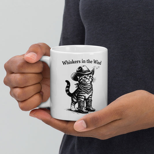 Person holding a white mug with a cat illustration and text 'Whiskers in the Wind' on a plain background