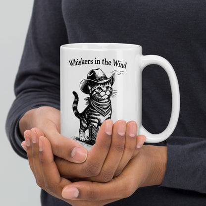 Person holding a white mug with a cat illustration and text 'Whiskers in the Wind' on a plain background