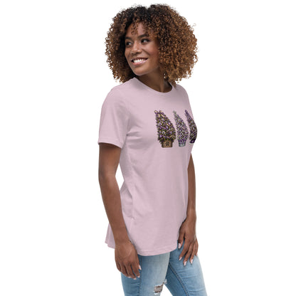 A woman with curly brown hair wearing a light pink long-sleeve t-shirt with a graphic of three potted topiary trees, paired with light blue jeans, set against a plain white background.