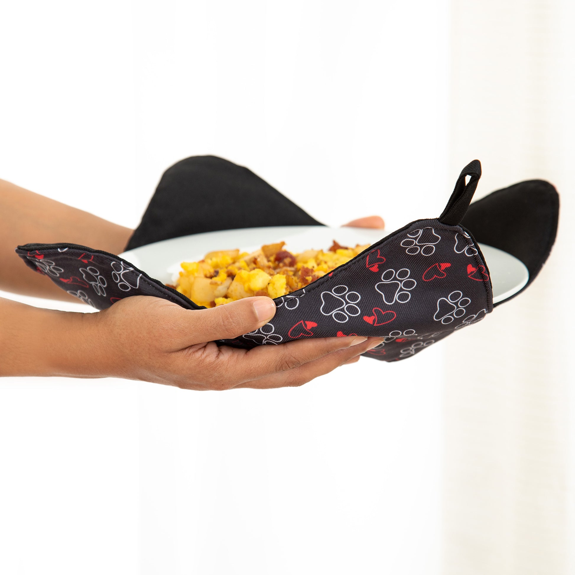 Hands holding a plate resting on a paw printed plate cozy, against a white background.